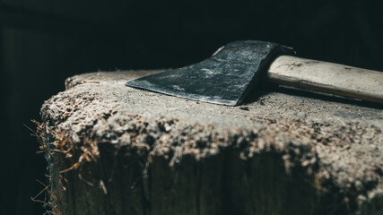 An axe with a wooden handle lies on a stump for chopping firewood in the black background