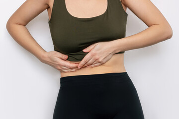 Cropped shot of a young slender woman holding her side with her hands isolated on a white background. Sore side under the rib after training. Stomach pain - obrazy, fototapety, plakaty