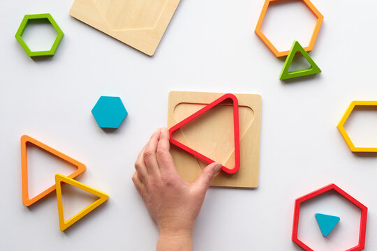 Hand with triangle. Nested wood triangles and hexagons, concentric figures. Stacking puzzle, Montessori nesting sensory gift for toddlers and kids. Flat lay, top view on white paper background.