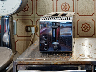 Dirty toaster with burnt crumbs on the kitchen table against the background of light tiles