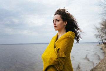 a woman stands on the shore of the lake covered with a yellow cape