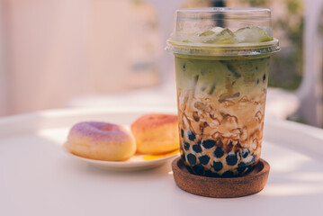 Iced matcha green tea latte with pearls in a take-away plastic cup and donut in a plate.Homemade...