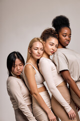 Balanced, calm diverse female models leaned on each other posing, looking down, isolated on beige studio background, portrait copy space. natural beauty, calmness, confidence concept