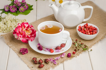 Herbal tea with rosehip and meadowsweet in a white cup on a white wooden table with flowers