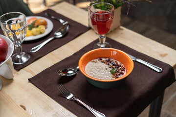 Oatmeal porridge in a orange porcelain bowl with jam and seeds.
