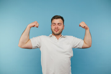 Fototapeta premium Strong adult man in white t-shirt shows biceps to camera and smiling, isolated on blue background.