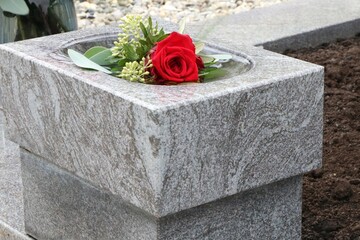 Rote Rose in einem Weihwasserbehälter an einem katholischen Friedhof in Österreich, Grabschmuck, Gedenkstätte, Erinnerung, Trauer, Tod, Bestattung