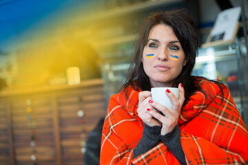 donna  con la bandiera dell'Ucraina disegnata sul viso si copre il corpo con un plaid mentre bene ...