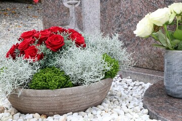 Blumenschmuck auf einem katholischen Friedhof in Österreich, Blumenschale mit roten Rosen, daneben eine Vase mit weißen Rosen