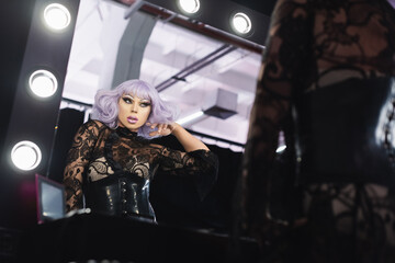 low angle view of glamour drag queen touching purple wig near mirror.