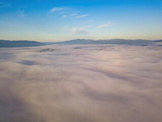 Obraz na płótnie Canvas Flight over fog in Ukrainian Carpathians in summer. A thick layer of fog covers the mountains with a solid carpet. Mountains on the horizon. Aerial drone view.
