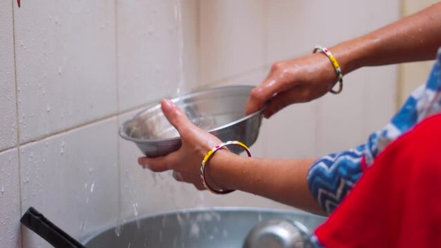 Close Up Of Rural Indian Woman's Hands Washing Utensils In Home. Making Homework. Domestic Life Concept In India. Hands Cleaning Dish With Flowing Tap Water. Cleaning Concept