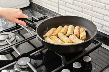 A woman fries pancakes in a pan on an electric stove in the kitchen.