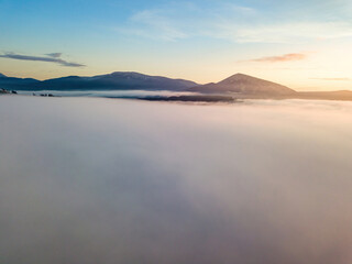 The rays of dawn over the fog in the Ukrainian Carpathians. Aerial drone view.