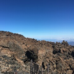 Blick vom Gipfel des Teide auf den Atlantik mit Schleierwolken im Tal und darüberliegendem blauen Himmel
