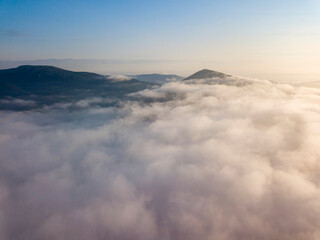 Flight over fog in Ukrainian Carpathians in summer. Mountains on the horizon. Aerial drone view.