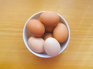 Colorful organic chicken eggs in a white bowl over a wooden table. Fresh product, local farm, sustainable and healthy lifestyle. View from above. 