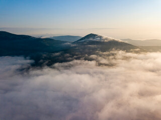 Flight over fog in Ukrainian Carpathians in summer. Mountains on the horizon. Aerial drone view.