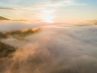 Naklejka na ściany i meble The rays of dawn over the fog in the Ukrainian Carpathians. Aerial drone view.