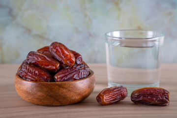 Glass of water with a bowl of date fruit on a wooden background