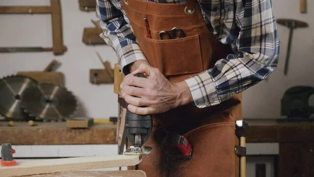 Carpenter is sawing a wood plank with electric jig saw machine in carpentry workshop. Workwood DIY concept. High quality 4k footage