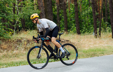 Professional athlete cyclist trains in the woods on an asphalt road. The man is engaged in triathlon.