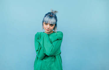 Cute hipster girl with blue hair isolated on blue background posing at camera in green sweatshirt.