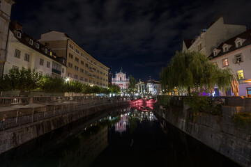 Fototapeta na wymiar Panorama of Ljubljanica river with the Tromostovje (triple most) rbidge in Ljubljana, capital city of Slovenia, taken during a summer night. this bridge is one of the symbols of the city