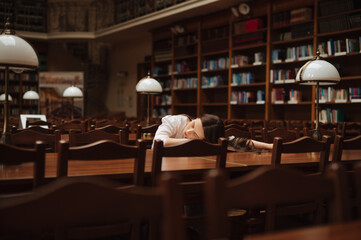 Female student fell asleep reading a book in a public library, lying on a book and sleeping.