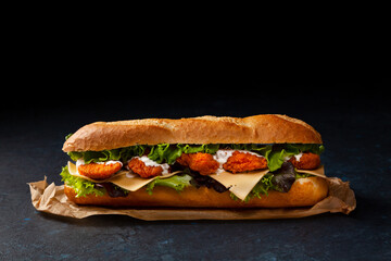 Chicken sandwich in breadcrumbs. A long roll. Dark mood.