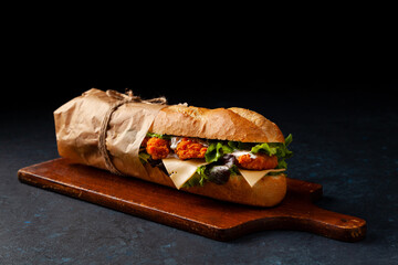 Chicken sandwich in breadcrumbs. A long roll. Dark mood.