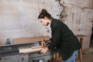 Side view of carpenter working with plank and jointer machine in workshop.