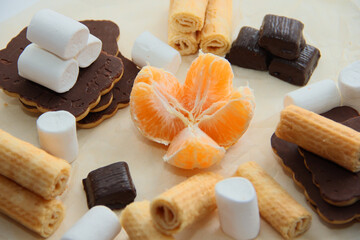 the choice of healthy or harmful sweets. chocolates, cookies, waffles, marshmallows and tangerine on parchment paper