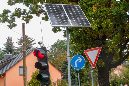 Rote Ampel neben einer Solaranlage, einem Rechtsabbiegeschild und einem Achtung-Verkehrsschild in Deutschland. Remote Stromversorgung im Straßenverkehr. Solarbetriebene Ampel mit Photovoltaikanlage.