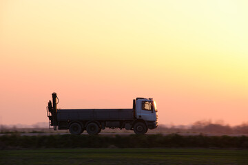 Cargo dump truck driving on highway hauling goods in evening. Delivery transportation and logistics concept