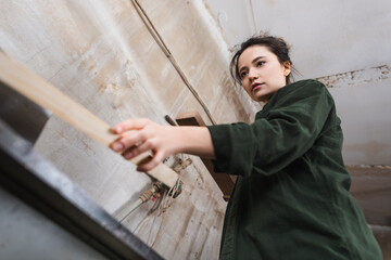 Naklejka premium Low angle view of carpenter holding blurred plank near jointer machine.