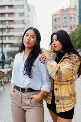 vertical portrait of two hispanic sisters together in the street. Friendship and family.