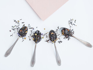 Dry black tea mixed with herbs for brewing is poured into spoons, rays diverge from the corner of beige paper. Mock-up for tea business.