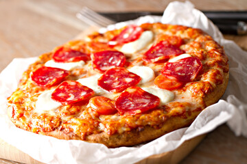 Pizza with pepperoni sausage and cheese on a wooden board on a wooden background