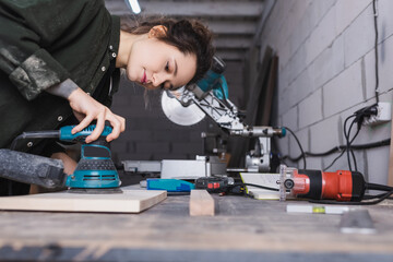 Carpenter using sander on wooden plank in workshop.