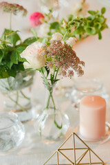 Coziness and style. Modern event design. Table setting at wedding reception. Floral compositions with beautiful flowers and greenery, candles, laying and plates on decorated table.