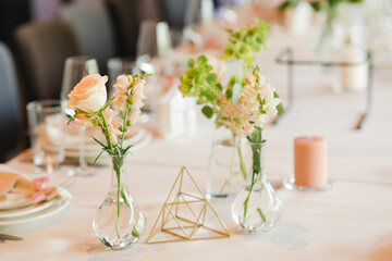 Coziness and style. Modern event design. Table setting at wedding reception. Floral compositions with beautiful flowers and greenery, candles, laying and plates on decorated table.