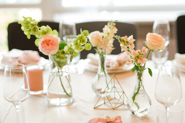 Coziness and style. Modern event design. Table setting at wedding reception. Floral compositions with beautiful flowers and greenery, candles, laying and plates on decorated table.