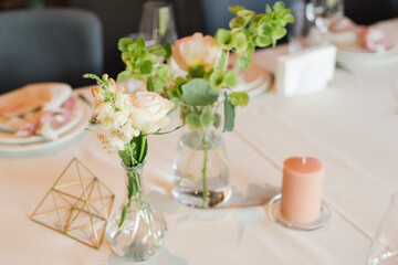 Coziness and style. Modern event design. Table setting at wedding reception. Floral compositions with beautiful flowers and greenery, candles, laying and plates on decorated table.