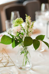 Coziness and style. Modern event design. Table setting at wedding reception. Floral compositions with beautiful flowers and greenery, candles, laying and plates on decorated table.