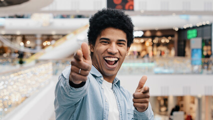 Hey you gesture indoor portrait african man pointing index fingers to camera indicating happily choosing smiling pistols shooting sign approve good idea select agree symbol funny male point with hands
