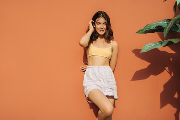 Fair skinned young caucasian woman straightens her dark hair while standing against red wall on...