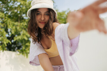 Portrait of young caucasian woman in summer light clothes stretches hand forward outdoors. Brunette...