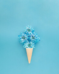 Ice cream cone with soft blue flowers like ice cream. Spring summer sunny days concept idea. Flat lay food aesthetic fashion design