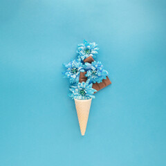 Ice cream cone with soft blue flowers like ice cream and chocolate. Spring summer sunny days concept idea. Flat lay food aesthetic fashion design